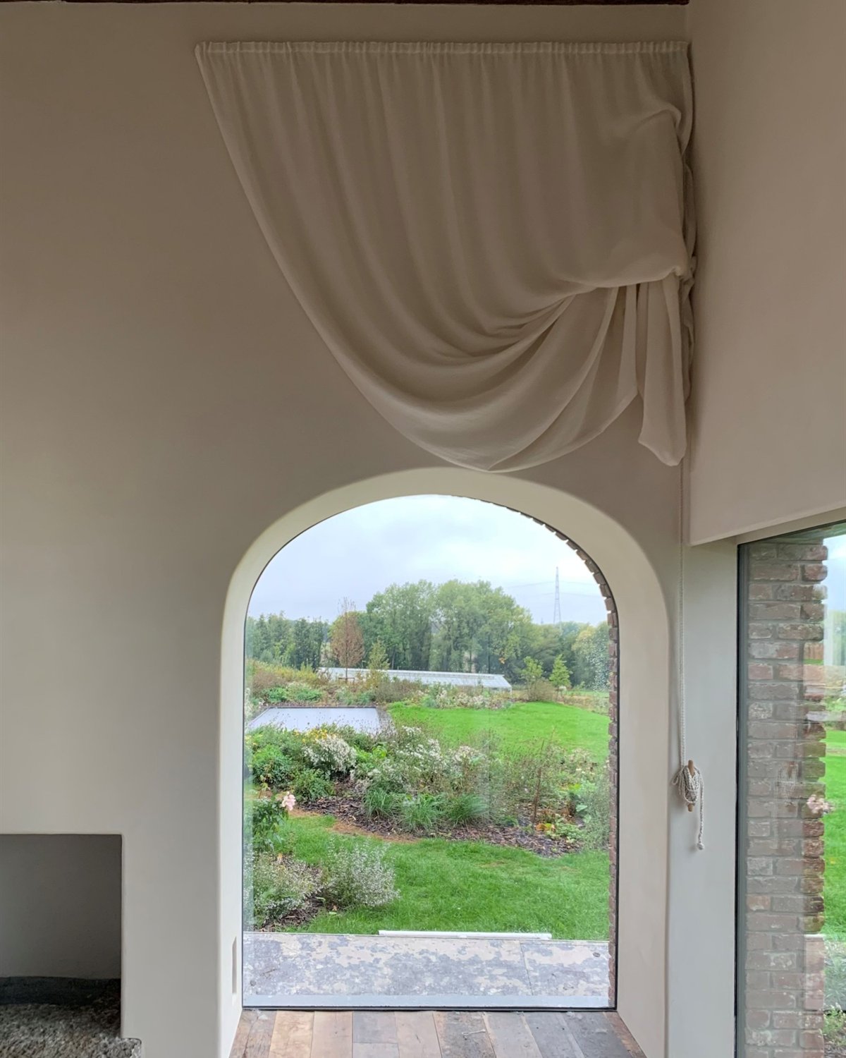 Opgenomen gordijn met knoop boven een boogvenster met zicht op de tuin
